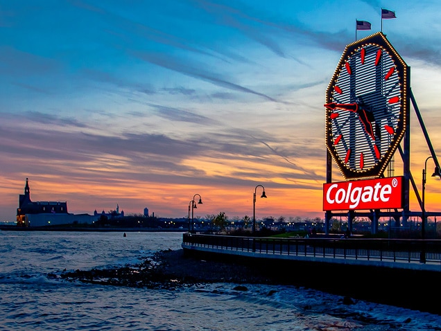 берег моря, логотип Colgate на тлі під великим годинником із червоними стрілками