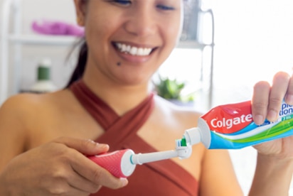 Жінка посміхається, наносячи зубну пасту «Colgate» на зубну щітку у ванній кімнаті.